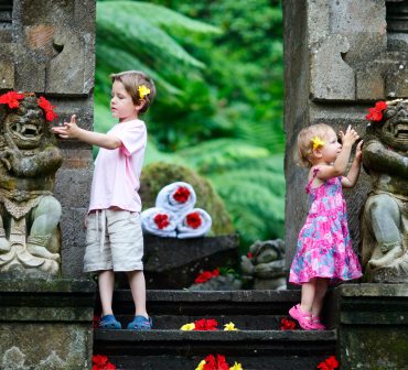 Brother and little sister, at a temple in Bali, looking at brightly colored flower petals